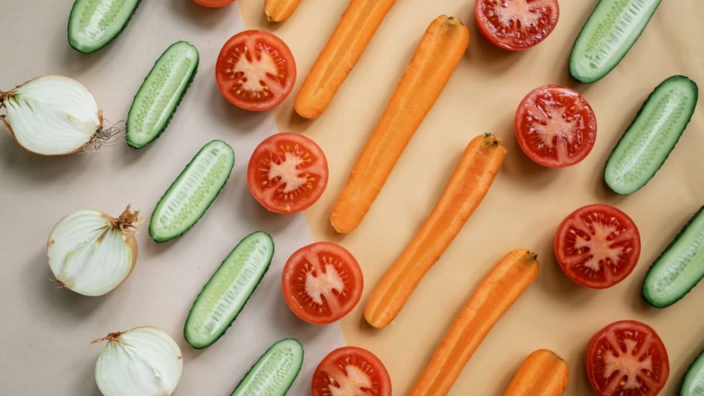 Top view of fresh sliced vegetables including carrots, cucumbers, onions, and tomatoes in a flat lay design.
